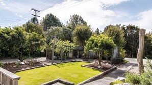 A backyard with a wooden deck, a grassy lawn, and various trees and shrubs. - Emily's Beach House - Kaiteriteri Holiday Home (Kaiteriteri)