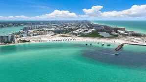 Una vista aerea di un resort costiero con spiaggia, acque turchesi cristalline e un porto turistico.