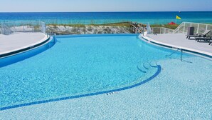 Una piscina azul cristalina con un muelle de madera y sillas de descanso, con vista a una playa y una bandera.