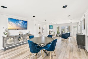 Un vaste espace dédié à la salle à manger, avec une table ronde et des chaises bleues, une console moderne agrémentée d’objets décoratifs et un grand tableau accroché au mur.