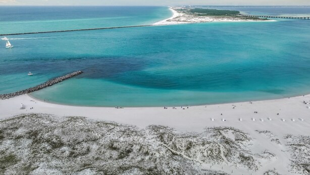 Una zona costera con playa, muelle y faro.
