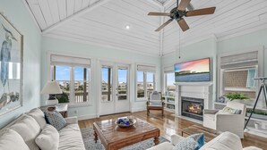 Un salón espacioso con techo alto, chimenea y televisor grande.
