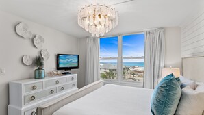 Un dormitorio con cama, cómoda, televisor y vista al mar.