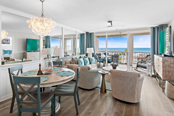 Un vaste espace de vie comprenant une salle à manger, des canapés et un balcon offrant une vue sur l’océan.