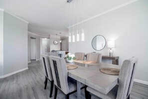 A dining area with a rectangular table, grey upholstered chairs, and pendant lighting. - Vista Cay Lakeview Elysium. Walk to Epic Universe and the OCCC (Orlando)