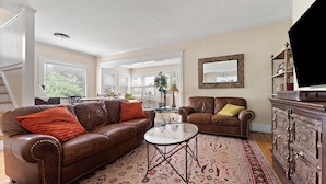 A spacious living room with two leather sofas, a glass coffee table, and a patterned rug.