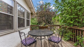 A wooden deck with a round table and four chairs, surrounded by a wooden fence and lush greenery.