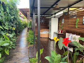 A covered outdoor area with a wooden deck, a wicker sofa, and a wall with a 'BEACH HOUSE' sign.