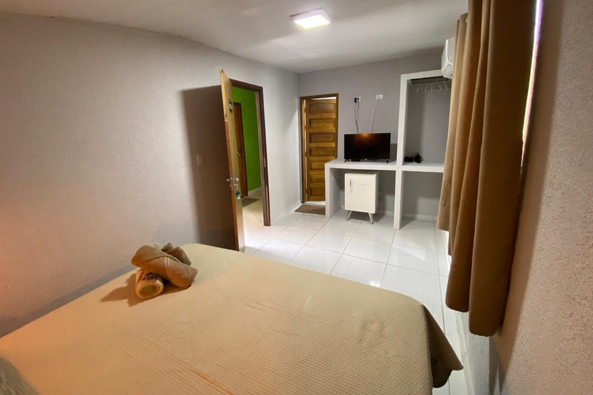 A hotel room with a bed, a desk with a television, and a door leading to another room.