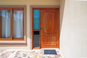 Uma porta de madeira com um painel de vidro e puxador de metal, uma janela com moldura de madeira e uma área de entrada com azulejos.