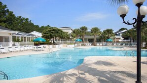 A swimming pool with lounge chairs and umbrellas, surrounded by palm trees and buildings. - 1st Level w/updates, family-friendly, 5 mins to beach, w/pool access, sleeps 6 (Sunset Beach)