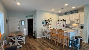 A compact kitchen with white cabinets, a wooden dining table, and a small island with stools. - 1st Level w/updates, family-friendly, 5 mins to beach, w/pool access, sleeps 6 (Sunset Beach)