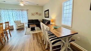 A dining area with a wooden table, white chairs, a black sofa, and a patterned rug. - 1st Level w/updates, family-friendly, 5 mins to beach, w/pool access, sleeps 6 (Sunset Beach)