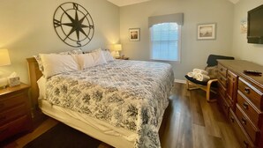 A bedroom with a large bed, a ceiling fan, a wall clock, and a window with blinds. - 1st Level w/updates, family-friendly, 5 mins to beach, w/pool access, sleeps 6 (Sunset Beach)
