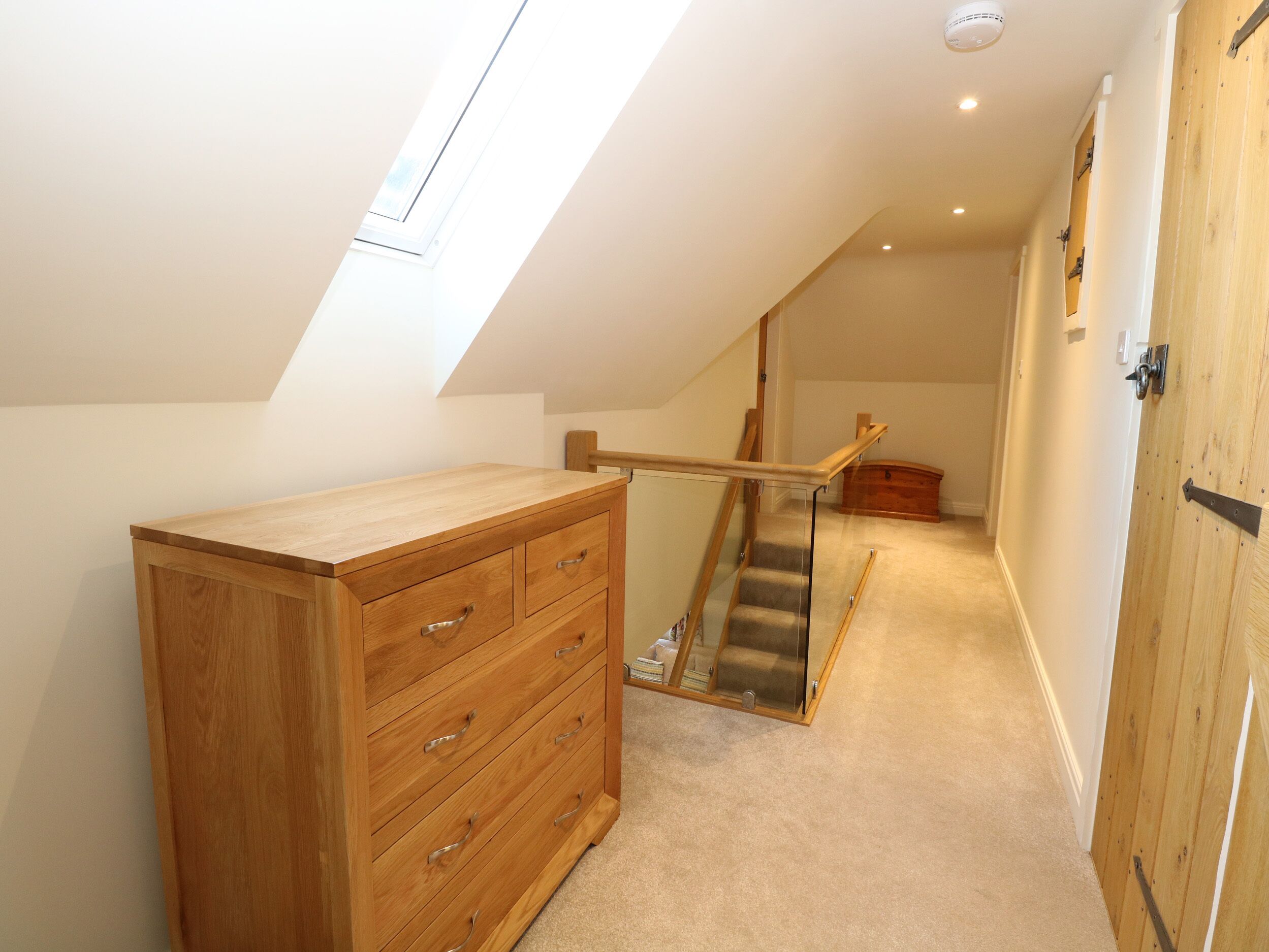 Una habitación con un aparador de madera, una escalera con barandilla de cristal y una puerta de madera.