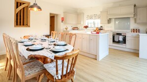 Une cuisine moderne avec des meubles blancs, un îlot central et un coin repas comprenant des chaises en bois et une table dressée pour six personnes.