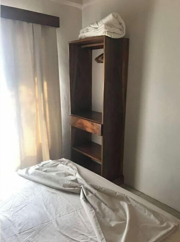 A room with a bed, a wooden wardrobe, and a window with curtains.