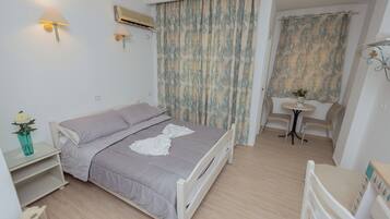 A bedroom with a bed, bedside table, lamp, air conditioning unit, curtains, and a small table with chairs.