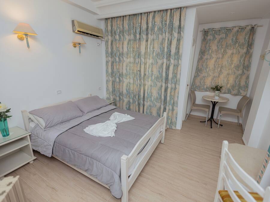 A bedroom with a bed, bedside table, lamp, air conditioning unit, curtains, and a small table with chairs.