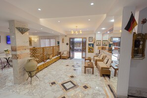 A spacious living area with a marble floor, a wooden sofa set, a small wooden table, and a decorative vase. - Hôtel Résidence Monia  (Sousse)