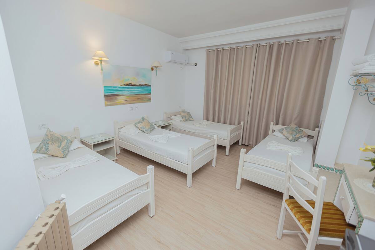 A room with three single beds, a chair, a small table, and a painting of a beach scene.