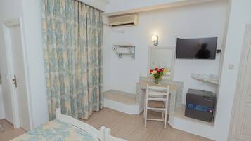 Une chambre comprenant un lit, un bureau, une chaise, une télévision, un radiateur et une petite étagère avec des articles de toilette.