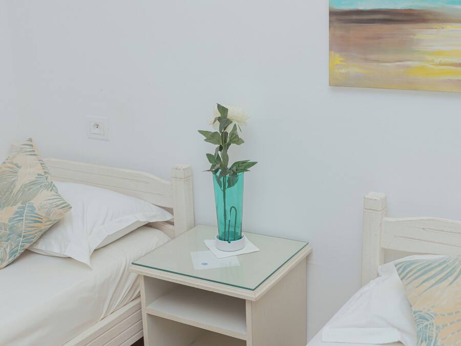 Una habitación con dos camas individuales, una mesita con un florero y un cuadro de una playa.