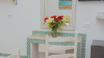 A small room with a white desk, a chair, a television, and a mirror.