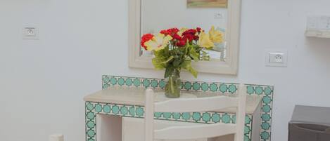 Une petite pièce avec un bureau blanc, une chaise, un téléviseur et un miroir.
