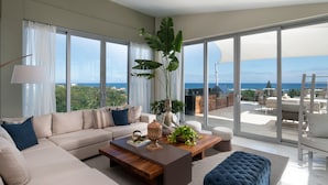 A modern living room with a large sofa, coffee table, and a view of the ocean through large windows. - Luxury Apartments - VIP All-inclusive (Puerto Plata)
