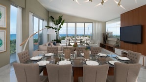 A modern dining area with a panoramic ocean view, a large round table set for six, and a television mounted on the wall. - Luxury Apartments - VIP All-inclusive (Puerto Plata)