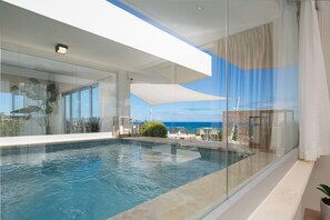 Una piscina infinita moderna con agua azul cristalina, rodeada de paredes de vidrio y un techo blanco.