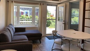 A cozy living room with a sofa, a round table, and a view of a garden through a sliding glass door. - Quarterboard 9 (Sandwich)