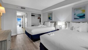 A hotel room with two beds, a desk, and a view of the balcony.