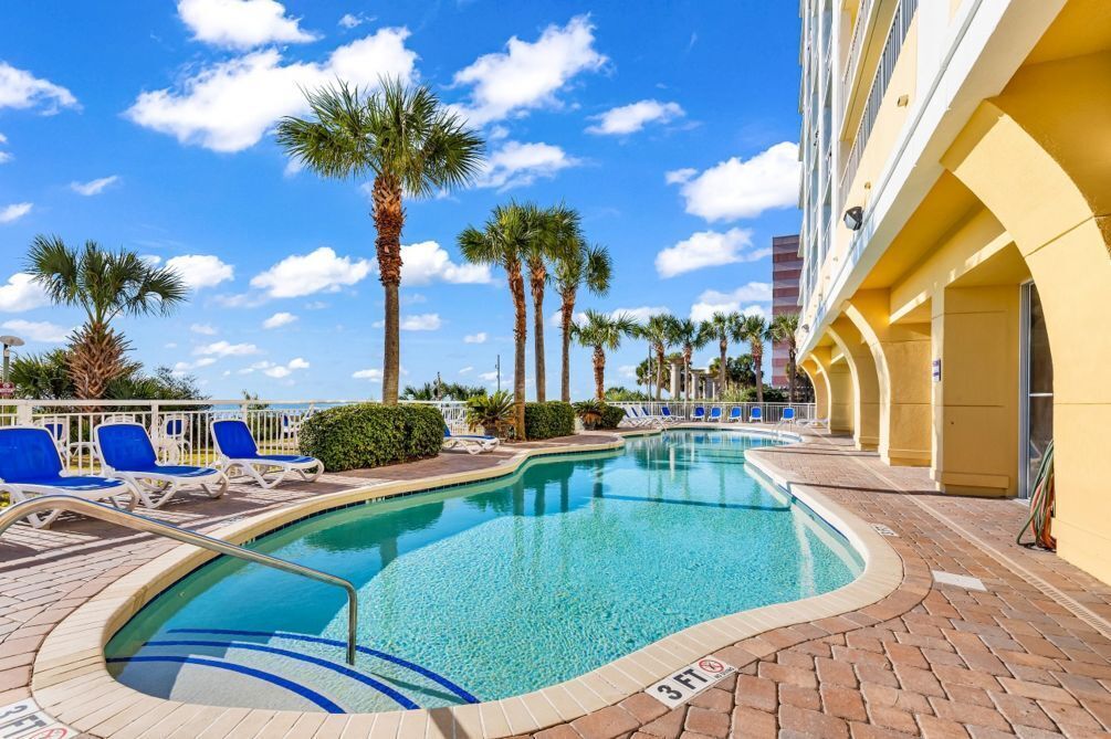 A swimming pool with lounge chairs, palm trees, and a building with yellow walls.