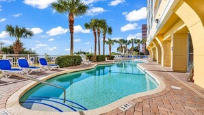 A swimming pool with lounge chairs, palm trees, and a building with yellow walls.