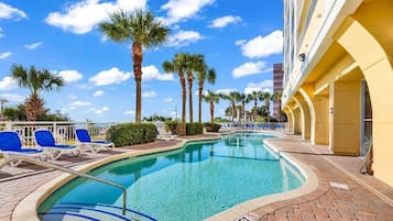 A swimming pool with lounge chairs, palm trees, and a building with yellow walls.