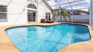 A swimming pool with a curved edge, surrounded by a covered patio area with outdoor furniture. - Cozy on Cavendish Themed Bedrooms (Kissimmee)