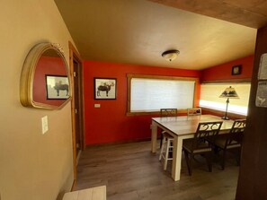 Uma sala de jantar com mesa e cadeiras de madeira, uma janela com persianas e um espelho na parede.
