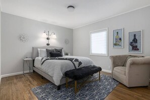 A bedroom with a bed, bedside table, lamp, chair, and artwork on the walls.