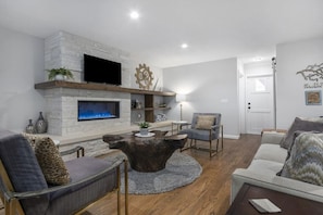 A modern living room with a fireplace, a flat-screen TV, and a coffee table.