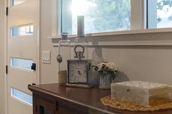 Una mesa de madera con un reloj, una botella de vidrio y un florero con flores.