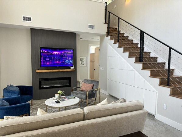 A modern living room with a flat-screen TV, a fireplace, a staircase, and a blue armchair.