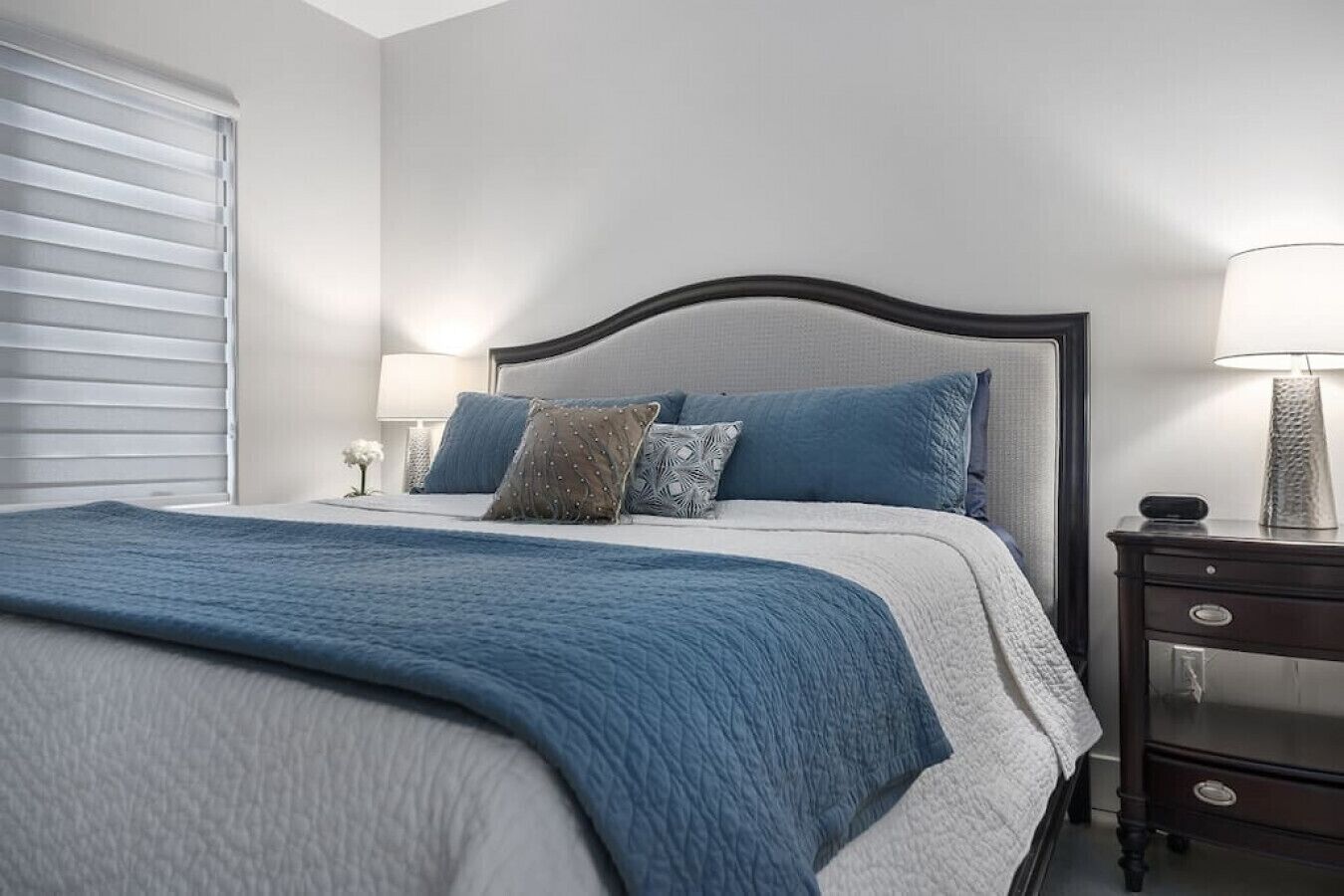 A neatly made bed with a blue blanket, a headboard, and two bedside lamps.