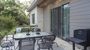 An outdoor patio with a glass-top table, metal chairs, a sofa, and a grill.