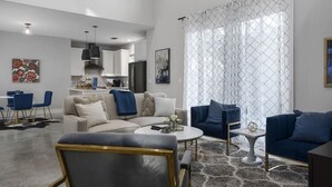 A modern living room with a sofa, armchairs, a coffee table, and a dining area with chairs and a table.