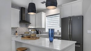 A modern kitchen with white cabinetry, a central island with stools, a large refrigerator, and pendant lighting.