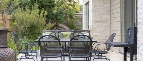 An outdoor patio with a table and chairs, a grill, and a potted plant.
