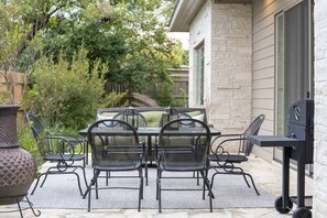 An outdoor patio with a table and chairs, a grill, and a potted plant.