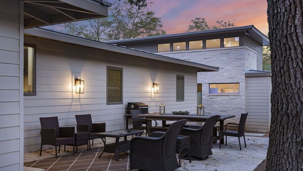 An outdoor patio area with a stone floor, dark wicker furniture, and a barbecue grill.